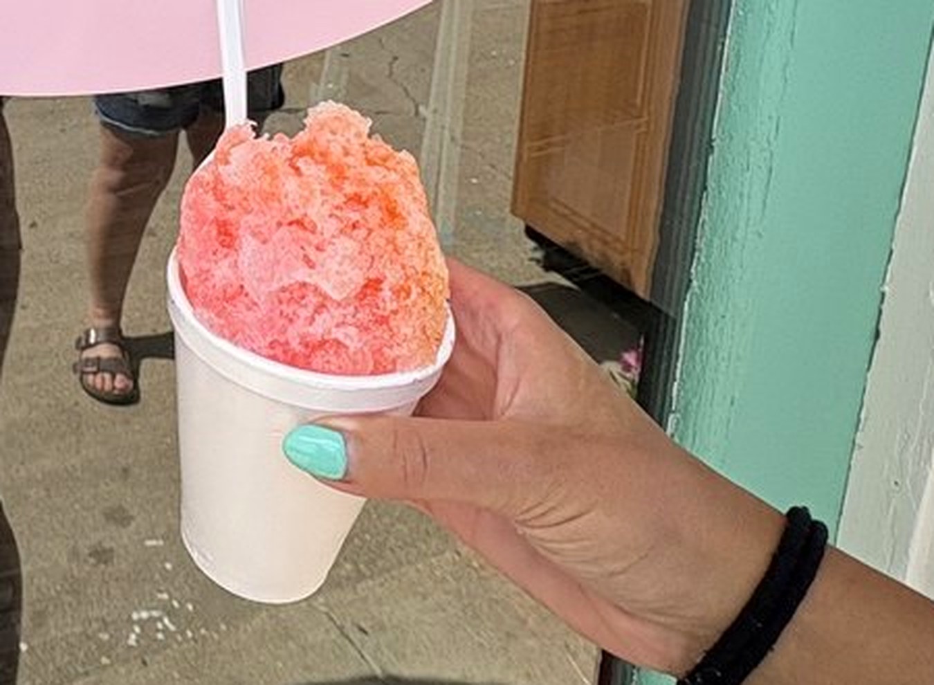 A large snow cone in a white cup, held outside the Shack
